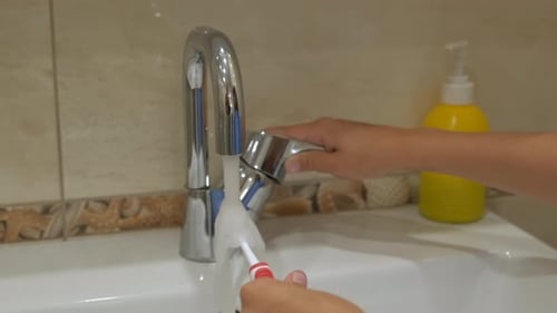 Toothbrush under running water in the sink.