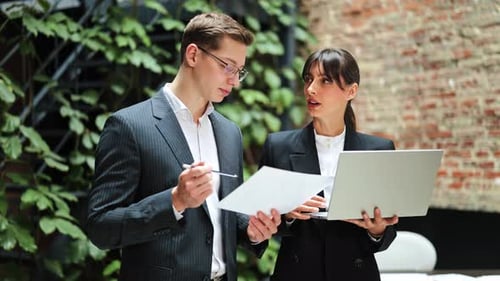 Business Partners in Suits Discussing a Project Using Laptop and Documents in a Modern Office