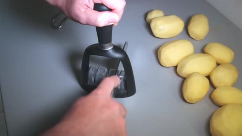 Zeitlupe von Menschenhänden beim Schärfen eines Küchenmessers auf einem Spitzer, geschälte Kartoffeln auf der Küchenplatte