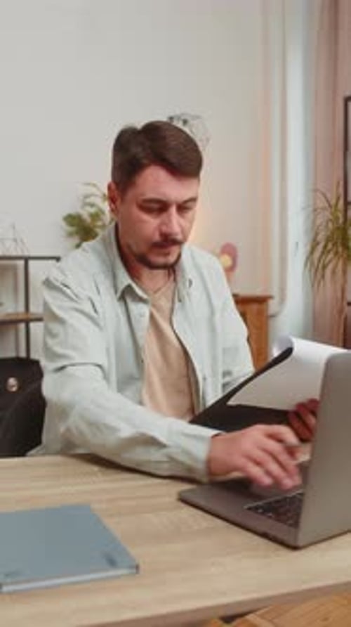 Caucasian Freelancer Accountant Working with Financial Graph Documents Using Laptop at Table Desk