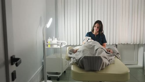 Skin Expert Using Electric Facial Brush On Masked Client Under Spa Lamp