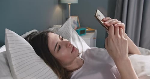 Beautiful Caucasian Woman Lying in Bed Click and Swipe on Phone Happy Smiling Female Spend Leisure