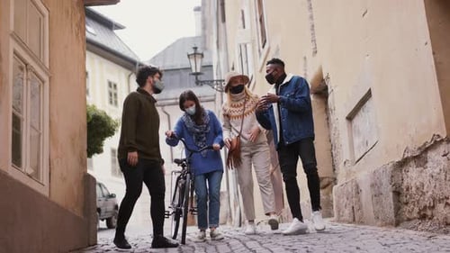 Multi-ethnic friends walk with bicycles in town during coronavirus pandemic