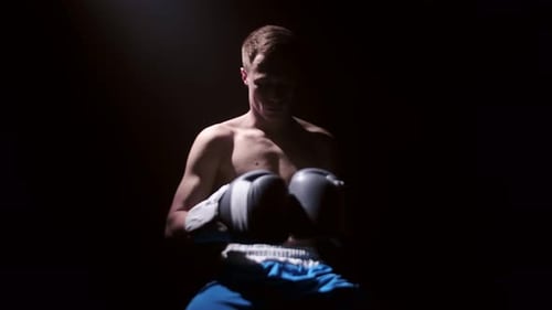 Taillenporträt eines jungen, fitten kaukasischen Boxers oben ohne, der mit seinen Händen in Boxhandschuhen auf einem