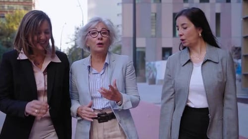 Three Mature Businesswomen Walking Outside Financial District Talking and Smiling Going to Work