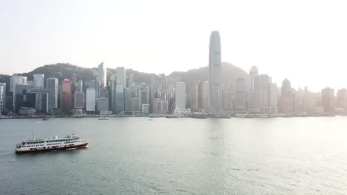 Aerial panning shot of boats in sea near city against sky at sunset, drone flying by modern building