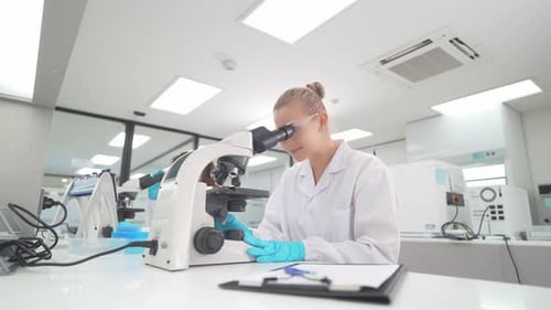 Female Scientist Works with Microscope in Bright Lab