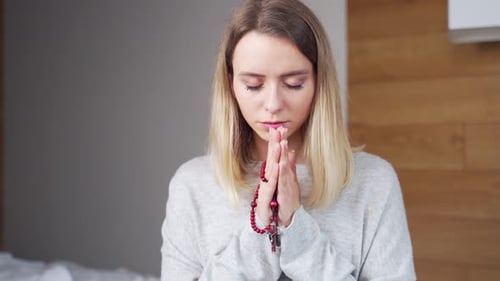 Woman Praying with Rosary Beads Indoors