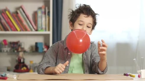 Young Boy Inflates Red Balloon at Home