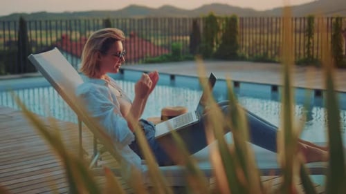 Frau mit blonden Haaren arbeitet an ihrem Computer am Resortpool