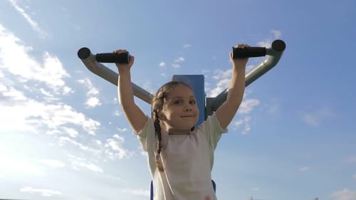 Little Adorable 5Yearold Girl is Engaged on Sport Simulator on the Street Playground in the Sunset