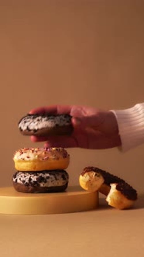 Hand Taking Donut from Stack with Bite Detail on Minimal Podium