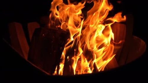 A slow motion reveal of a camp fire burning at night.