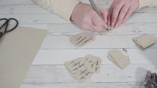 Woman Writes on Paper Tags at Table