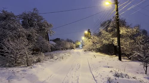 Camera Moving Along Snowy Country Road at Evening Time Street Lamp Illuminating Snow Trail at Winter