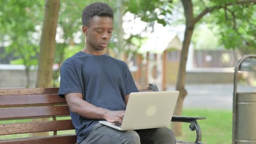 Young Adult Using Laptop on Park Bench