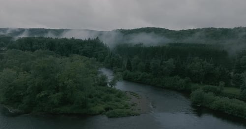 Drone flying through a beautiful foggy mountain top landscape, over a river. Straight and slight tur