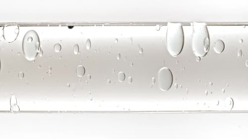 Gel fluide cosmétique transparent avec bulles de molécules et huile circulant dans un tube en verre avec liquide transparent