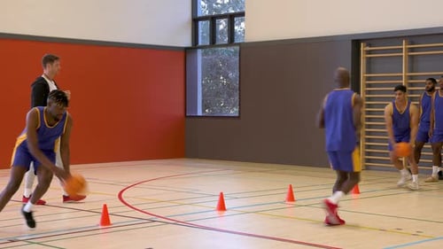 Basketball players practicing dribbling skills in gym with coach encouraging