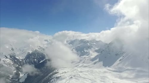 High in the Alps, a snowy mountainside and clouds at the peaks - aerial