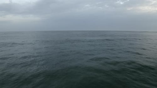 Waves washing onto sandy beach, overcast sky. Aerial forward at low altitude over water sea surface