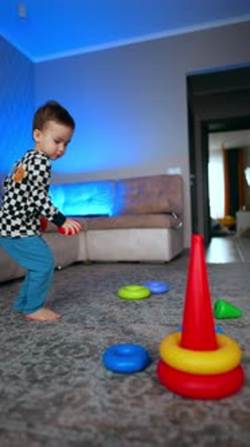 Un niño caucásico pasa por la habitación recogiendo sus juguetes. Lindo niño activo que construye una pirámide
.