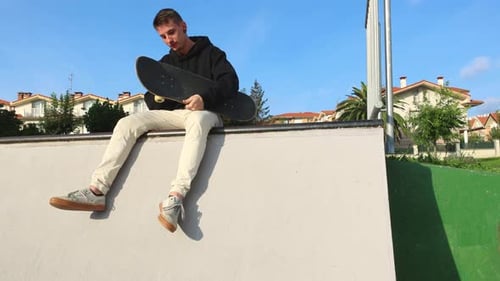 Skater Sitting on the Edge of the Half Pipe Checking His Board Wheels