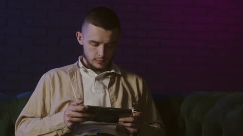 Man Plays Handheld Console in Neon-Lit Room