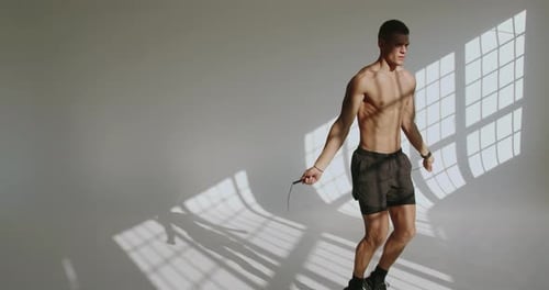 Junger athletischer Mann beim Seilspringen im sonnenbeschienenen Studio