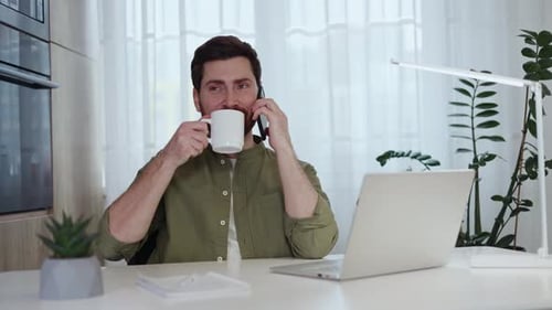 Man Talking on Phone and Drinking Coffee at Home