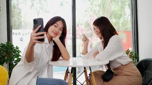 Asian woman and friend using smartphone selfie together in coffee shop.
