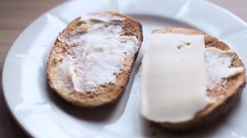 Person laying two slices of cheese on each bread. Preparing food on a white plate with slight zoom o