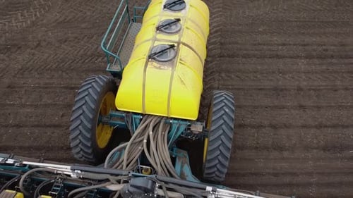 Blue tractor with yellow seeder working on the field in Ukraine OA