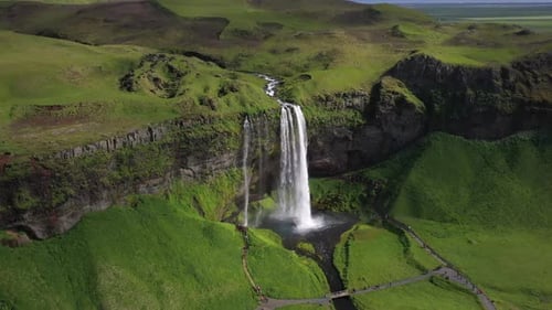 Spectacular Waterfall Plunges Down Vertical Cliff Amidst Vibrant Green Icelandic Scenery