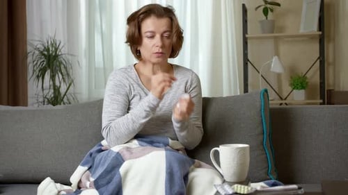 A cold and sick young woman with a runny nose sits on a sofa.