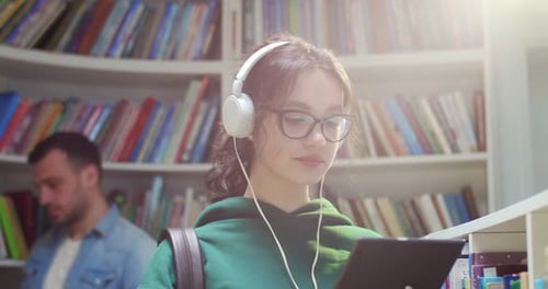 Close Up of Young Female Student in Glasses and Headphones Using Tablet Device and Tapping on Screen