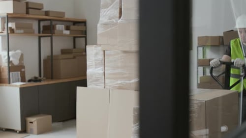 Storehouse Operative Pushing Manual Forklift with Heavy Boxes Wrapped in Film