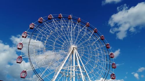 Ferris Wheel Spins Against Blue Sky and Clouds