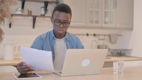 Young Adult Concentrating on Laptop and Papers at Home