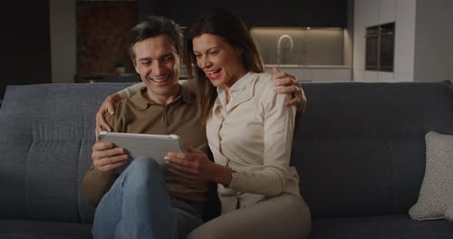 Couple Smiling While Looking at a Tablet on Couch