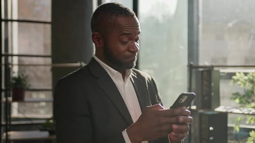 Smiling Mature Businessman in Sunny Office Using Mobile Phone Thoughtful African American Man