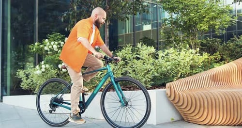 Handsome bearded smiling man riding bicycle at downtown district. Professional young male going