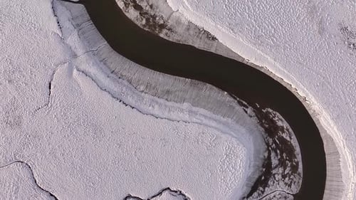 Aerial top-down view of a winding river through snowy terrain near Borgarfjörður, Iceland, with stri