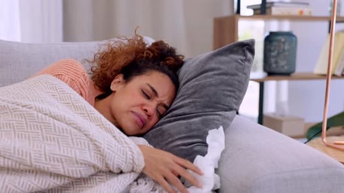 Malade, mouchoirs et femme se relaxant sur un canapé dans le salon de sa maison moderne pendant sa convalescence