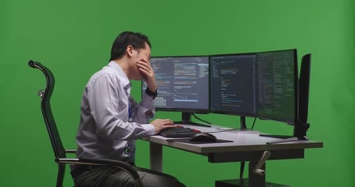 Tired Asian Man Developer Yawning While Write Code With Multiple Computer Screens In Green Screen