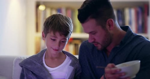 Father and Son Eating Noodles Together on Couch