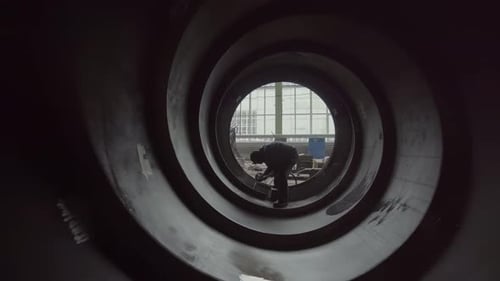 Ein Industriearbeiter wird in einem großen Rohr in einer geschäftigen Fabrikumgebung gesehen, einem Lagerbestand