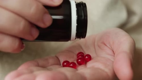Close-up of woman pouring red pills into hand
