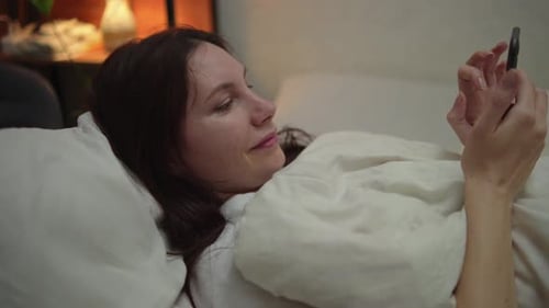 Woman Relaxes in Bed with Smartphone