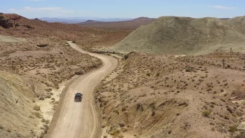 Black SUV 4x4 speeds down a dry dirt road in the desert leaving behind a dust trail; drone following